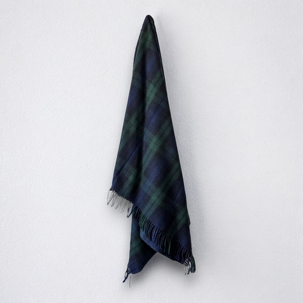a 100% recycled blanket in blackwatch tartan hanging from a wall hook on a white background 