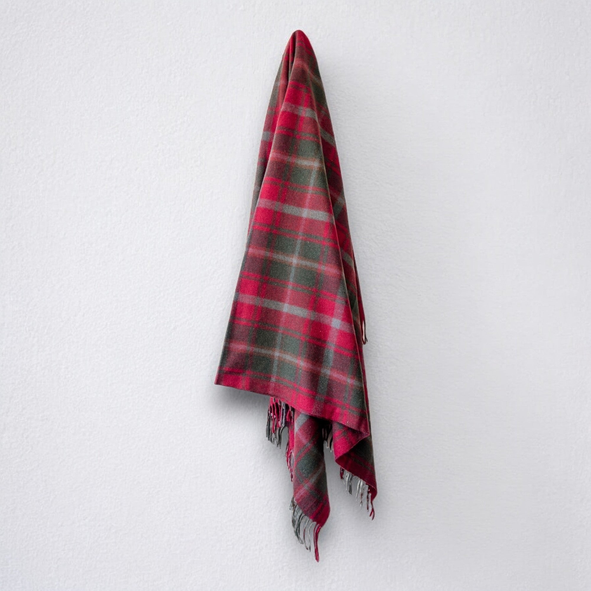 a 100% recycled blanket in maple tartan hanging from a wall hook on a white background 