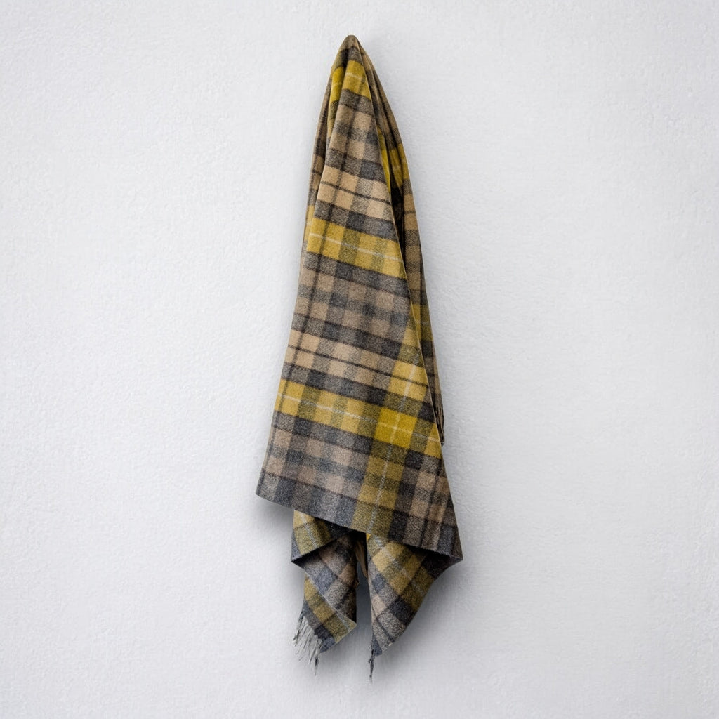 A recycled wool tartan blanket with fringed edges, draped over a white wall.