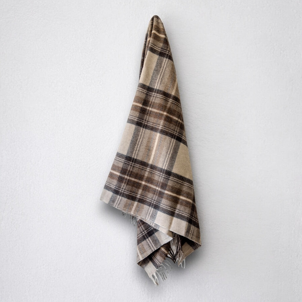 a 100% recycled blanket in natural dress tartan hanging from a wall hook on a white background 
