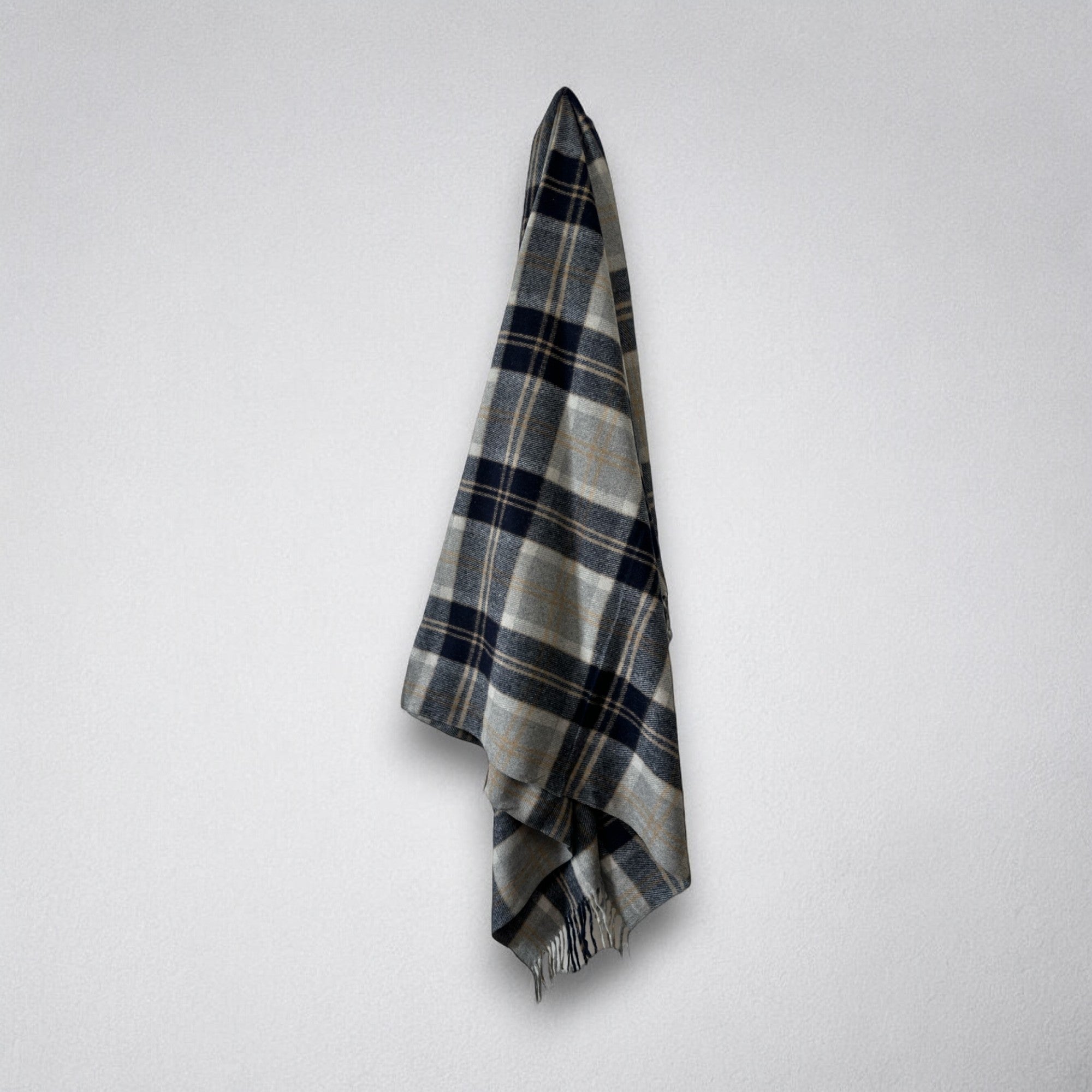 A Silver Bannockbane tartan patterned blanket draped over a white wall, with fringing visible on the ends.