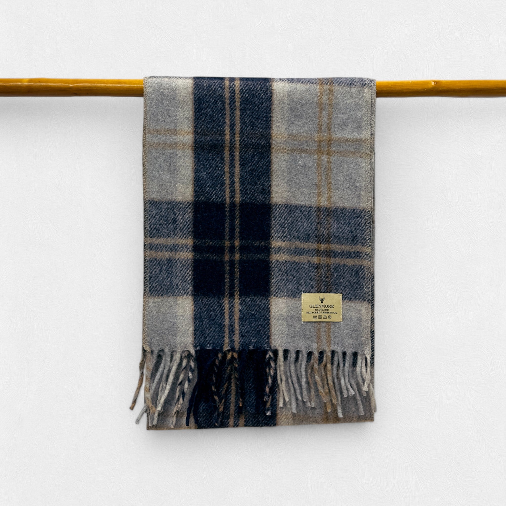 A silver bannockbane scarf with fringes, displayed on a yellow rod against a white wall.