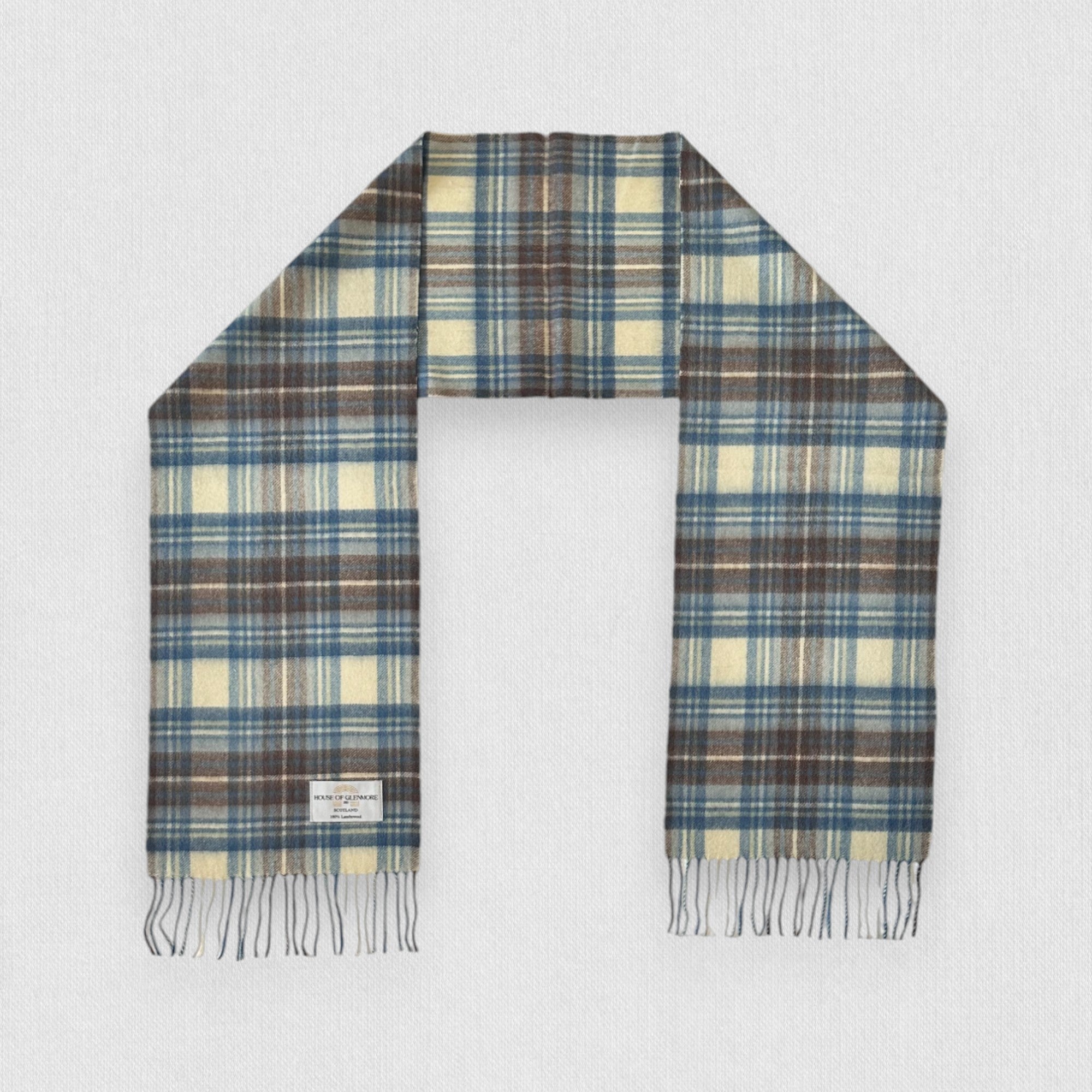 A Stewart Muted Blue tartan scarf made of 100% lambswool, displayed flat with fringes, showing the pattern of blue, grey, and white checkers.
