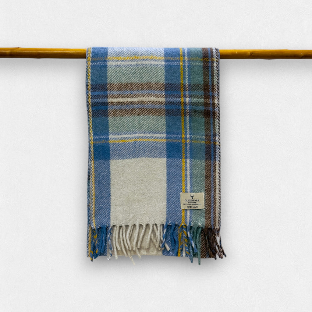 A plaid patterned scarf in stewart muted blue, green, and beige, displayed on a horizontal rod, with a label showing the brand name.