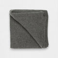 A folded dark grey cashmere blanket displayed on a surface.