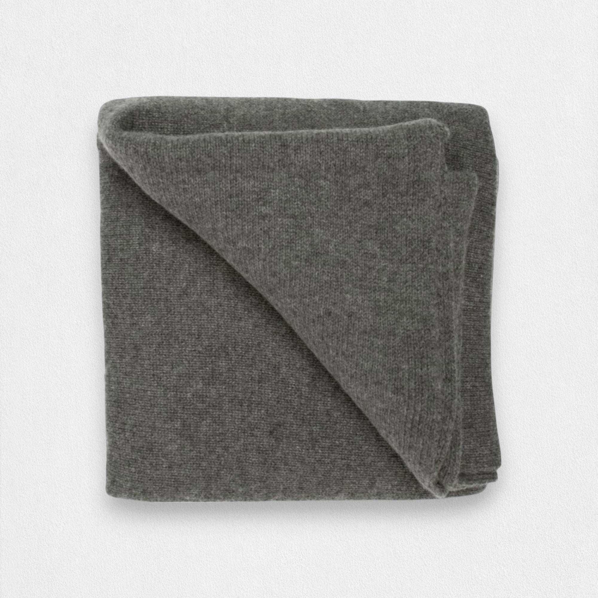 A folded dark grey cashmere blanket displayed on a surface.